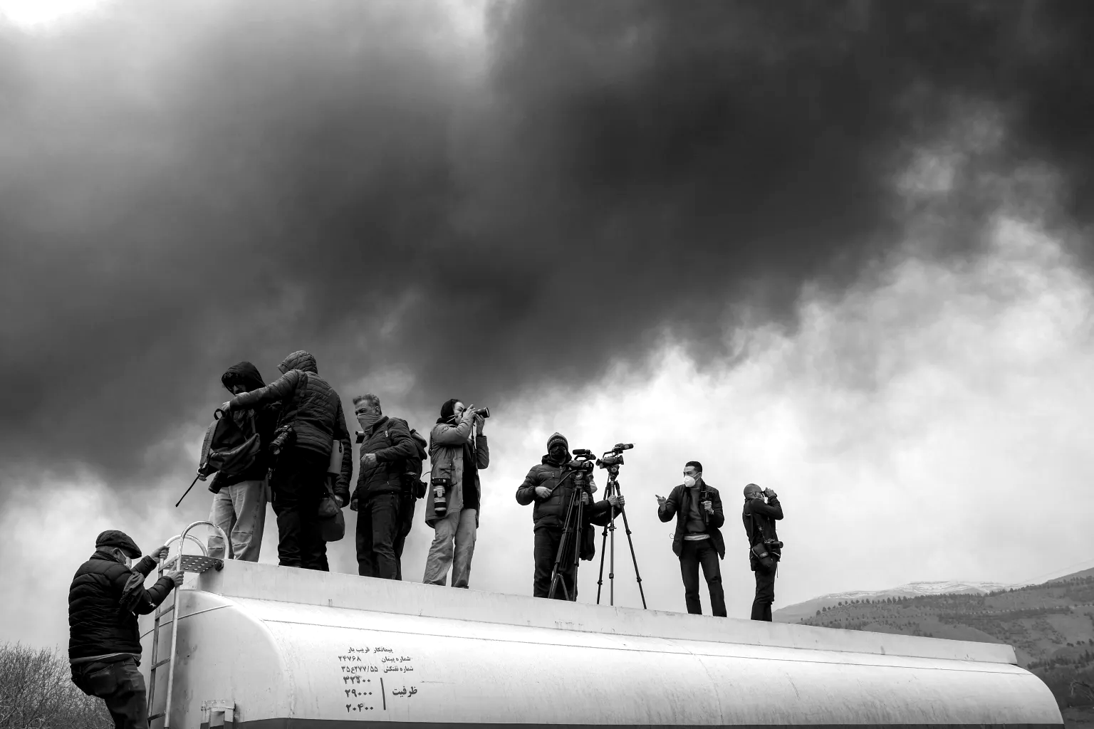 Journalists stand atop a fuel tanker as they cover a nearby fire following an overnight airstrike